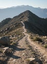 A winding dirt path leads through a rugged mountain landscape under a clear blue sky Royalty Free Stock Photo