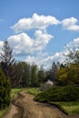 Winding dirt road in arboretum against background of blue sky with fluffy white clouds. Close-up. Royalty Free Stock Photo