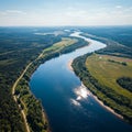 Winding river surrounded by dense forests and open fields, under a clear blue sky. Th Royalty Free Stock Photo
