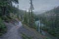Winding road leading to a misty forest by a river in the mountains. Foggy day in Jasper National Park, Alberta, Canada. Path into Royalty Free Stock Photo