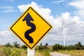 Winding road sign with windmill background in wind farm. Royalty Free Stock Photo