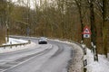 Winding road in winter with snow and a car approaching a slippery road sign Royalty Free Stock Photo