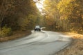 Winding rual road inside colorful autumn forest with black car Royalty Free Stock Photo