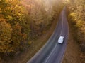 Winding rual road inside colorful autumn forest with car