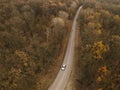Winding rual road inside colorful autumn forest with car