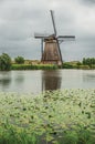 Windmill and bushes on the bank of a large canal in a cloudy day at Kinderdijk.