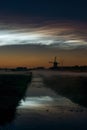 Noctilucent clouds over a classic dutch landscape at night with windmill along a canal. Royalty Free Stock Photo