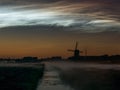 Windmill, fog banks and bright noctilucent clouds NLC over the dutch landscape during a midsummer night