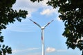 Windmill for generating electrical energy, framed from below by green leaves on branches Royalty Free Stock Photo