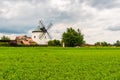 Windmill near the field with growing plant. Agriculture rural scene. Cloudy weather after rain, dramatic storm clouds