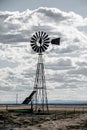 Windmill on the plains, powered by solar panels with livestock watering tank by barbed wire fence with mountains on horizon-