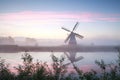 Windmill by river at misty sunrise