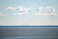 Windmills on the horizon with clouds in clear sky and sea in the foreground. Wind turbines, wind farms making electric power, Royalty Free Stock Photo