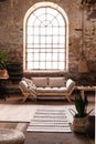 Window above grey wooden sofa in spacious loft interior in wabi sabi style with plant and carpet