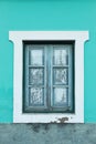 A window of a bright aquamarine, turquoise color house with an old wooden frame and a white paint around it Royalty Free Stock Photo