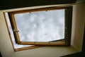 Window in the ceiling. Blue sky with clouds. Attic interior