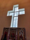 Window in a Christian church in the form of a cross. Below it are three icons. Tree branches outside the window