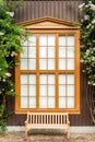 Window with curtains and shutters on a wooden house from boards with flowers and a bench Royalty Free Stock Photo