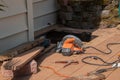 A window cut into brown wooden deck in order to repair a drainage problem under the deck. There are various power tools on the