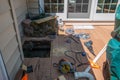 A window cut into brown wooden deck in order to repair a drainage problem under the deck. There are various power tools on the.