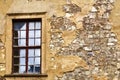 Window with frame from which the paint is peeling off, in a wall of hewn natural stone from which the plaster is falling off Royalty Free Stock Photo