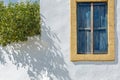 The window of a Greek house on a white wall with yellow trim and blue wooden shutters Royalty Free Stock Photo