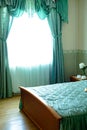 Window with green curtains in the bedroom with a bed, bedside table and cups Royalty Free Stock Photo