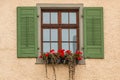 Window with green shutters and a flower box with red flowers Royalty Free Stock Photo