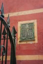 window with green shutters and fragment of a forged fence on ancient red textured facade of an old house Italy Royalty Free Stock Photo