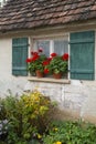 Window and green shutters of an old house with flower pots filled with red geranium flowers Royalty Free Stock Photo