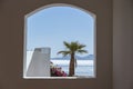 Window hole in the white stone wall of a building overlooking the Red Sea and a palm tree on a tropical beach in resort town Sharm Royalty Free Stock Photo