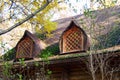 The window of an old wooden hut among the trees. Round carved window with wooden lattice on the roof of an old wooden