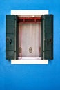 Window with opened green shutter on blue wall. Italy, Venice, Burano