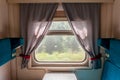 A window and part of the interior of a compartment car inside a traveling train in summer