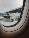 Window of a plane with view of airport gate bridge and terminal.