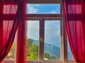 Window of a room with red curtains and a beautiful hill view in the background Royalty Free Stock Photo