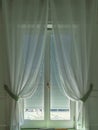 Window with translucent white curtains held on the side by light green strips on a white shutter, Massa Lubrense, Italy. Royalty Free Stock Photo