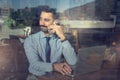 Through window view of handsome young businessman talking on mobile phone while working on laptop in office. Royalty Free Stock Photo