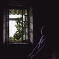 Window view from inside an old uninhabitable house and a blurred silhouette of a man. Depression, loneliness, despair, decline,