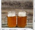 Window view of two pints of fresh cold beer on top of wooden crate with rustic wood in background Royalty Free Stock Photo