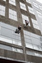 Window washers on top. Two workers hung ropes wash windows on high-rise