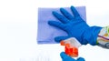 A female hand in a blue rubber glove wipes the window with a rag and detergent in the form of a spray.