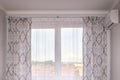 A window with a white tulle and a light curtain in an air-conditioned room overlooking the city. Interior and decoration