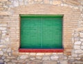 Closed window with wooden green shutters and a red windowsill in the old stone wall of the house Royalty Free Stock Photo