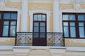 Windows and balcony with openwork wrought iron bars. Part of the facade of a yellow and white restored building. Beautiful Royalty Free Stock Photo
