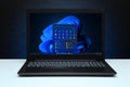 Windows 11 Desktop with logo on the screen laptop computer on black textured wall with blue light. Royalty Free Stock Photo
