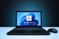 Windows 11 logo on the screen laptop computer with mouse on black textured wall with blue light. Royalty Free Stock Photo
