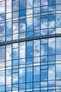 Windows of a skyscraper with reflection of blue sky and white clouds. A fragment of a glass facade of a modern office building in