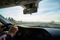 Windscreen view of nature, road, sky and hand of man on the steering wheel in a spring, summer or autumn day. The concept of a