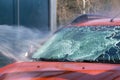 Windshield of car under powerful stream of water. Cleaning with water at self-service car wash. Soapy water runs down